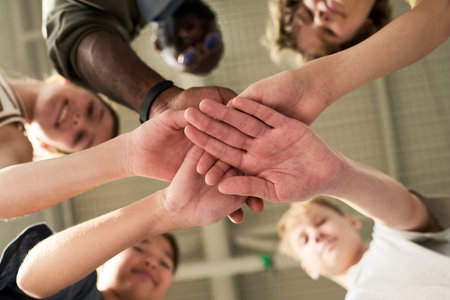Diverse group of teenagers stacking hands in unity, viewed from below, including Caucasian, Black,...