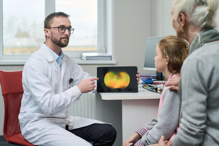 Caucasian male doctor showing retinal scan on digital tablet to senior Caucasian woman and Caucasian girl during medical consultation in clinic, doctor explaining diagnostic resultsの写真素材