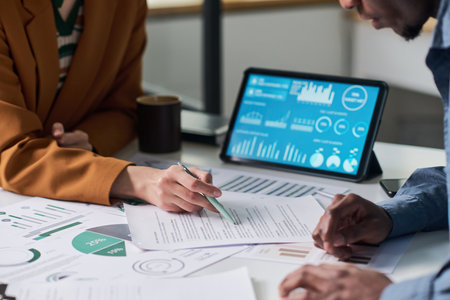 Caucasian young adult woman and Black man analyzing financial documents and discussing data with digital tablet displaying charts and graphs on office deskの写真素材