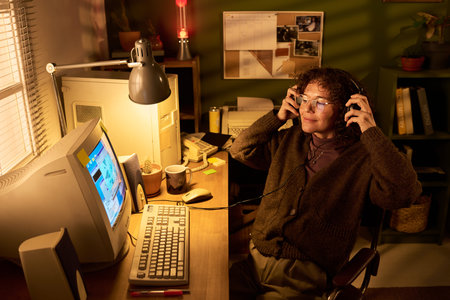 Caucasian woman sitting at desk using vintage desktop computer, wearing headphones and smiling,...