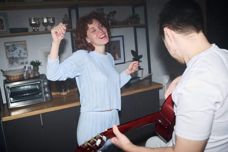 Caucasian young woman dancing with eyes closed while smiling, Caucasian young man playing acoustic...