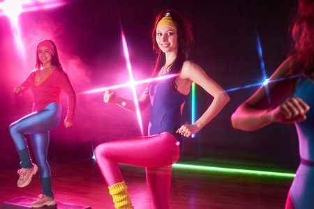 Group of young adult women exercising in fitness studio, performing aerobic step workout in colorful...