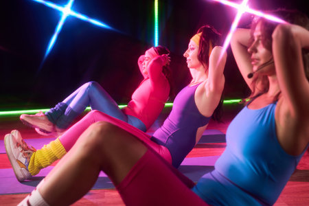 Three young adult Caucasian women exercising together on yoga mats performing sit ups in fitness...