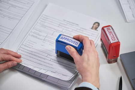 Close-up of female hand stamping visa application form with approved stamp at visa center, rejected...
