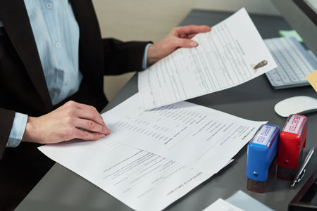 Unknown woman processing visa application documents at desk, holding paperwork with identification...
