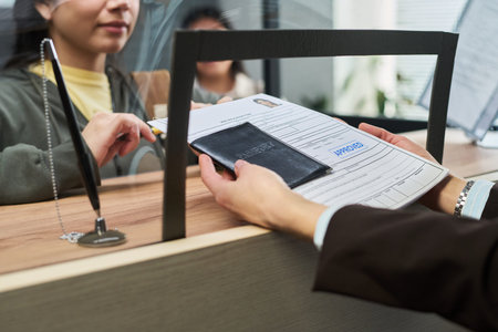 Woman handing passport and approved visa application to girl behind counter at visa center, both...