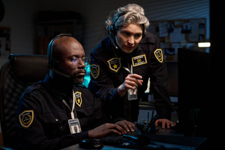 Black man wearing headset monitoring computer screen while Caucasian middle aged colleague standing...