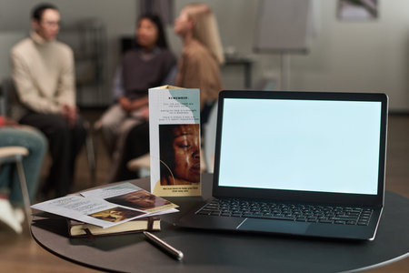 Open laptop with blank screen standing on table near brochures and notebook, background showing...