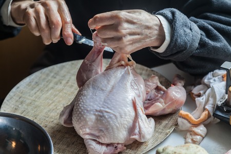 Hand with knife cutting chicken meatの写真素材