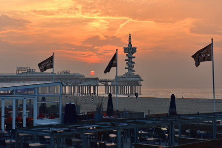 SCHEVENINGEN - SEPTEMBER 19: Sun setting behind the pier and restaurants along the sandy beach of Scheveningen, popular for water sports, taken on September 19, 2014 in Scheveningen, Netherlandsのeditorial素材