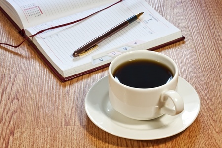 Coffee cup, pen, opened organizer, standing on the wooden tableの写真素材