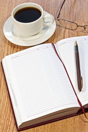 workplace at morning: coffee, notebook, pens, glasses on the table の写真素材