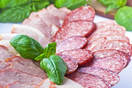 Cutting sausage and cured meat with a basilの写真素材