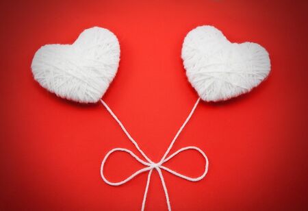 Two white hearts made from wool on red backgroundの写真素材