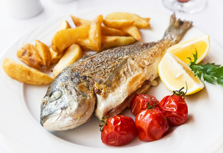 Fried fish dorado with potatoes chips, fresh herbs and lemon