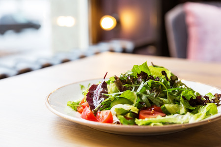 Fresh vegetable salad with tomato, cucumber, onion, spinach, lettuce and arugula on white plate. Bowl of salad with vegetables on wooden table.の写真素材
