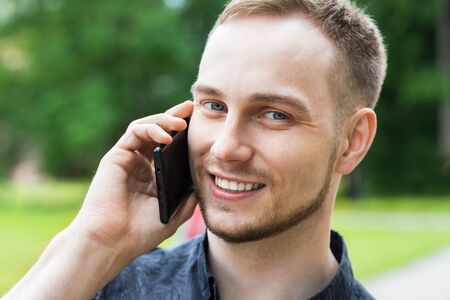 Portrait of handsome young male walking in the Park and talking on mobile smart phone. Man talking...