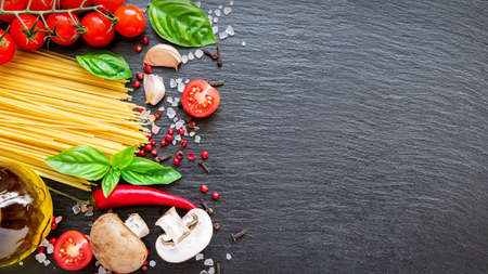 Food ingredients on dark background. Tomatoes, spaghetti, spices, garlic and basil leaves on black...