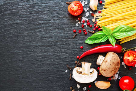 Tomatoes, spaghetti, spices, garlic and basil leaves on black background. Italian food, health or cooking concept. Food ingredients on dark background.の写真素材