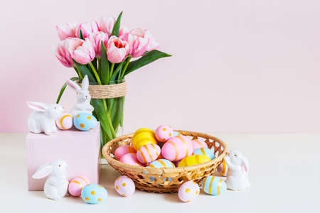 Easter and spring holiday greeting card concept. Pink tulips, easter bunnies with colorful eggs in basket. Painted Easter eggs in nest and tulips with white bunny, space for text. copyspace.の写真素材