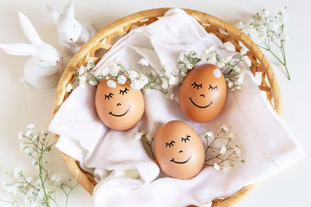 Three happy Easter eggs with cute faces in floral wreath crowns on white background in nest and two...