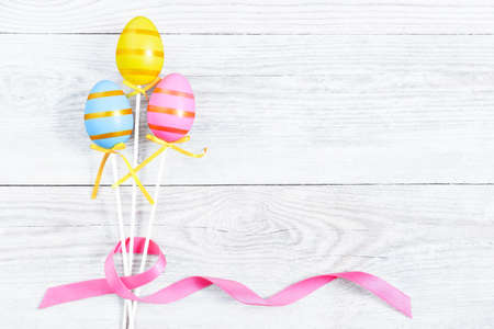 Three colorful Easter egg with pink ribbon bow on blue old wooden table. Light blue Easter background and copy space. Modern greeting card for the celebration of Easter.の写真素材