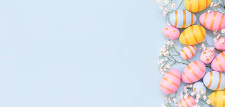 Easter holiday background with colorful easter eggs and white flowers on blue background. Top view...