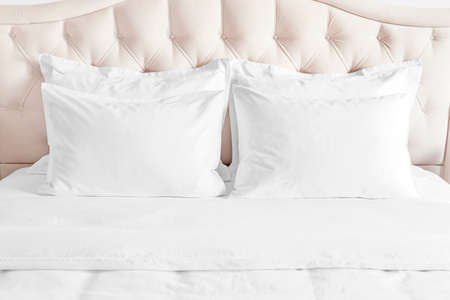 Bedroom with bed and white bedding White pillows, duvet and duvet case on bed with beige headboard. Bed with clean white pillows and bed sheets in beautyful bedroom.の写真素材