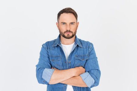 Portrait of young handsome serious man confident crossed hands, isolated on gray background. Bearded man looking at camera with serious expression, determined business man.の写真素材