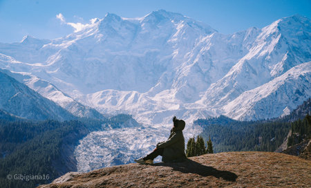 In an incredible moment, a woman sits on the ground, gazing upwards at the vast sky, with a towering snow-covered mountain serving as a breathtaking backdrop.の素材