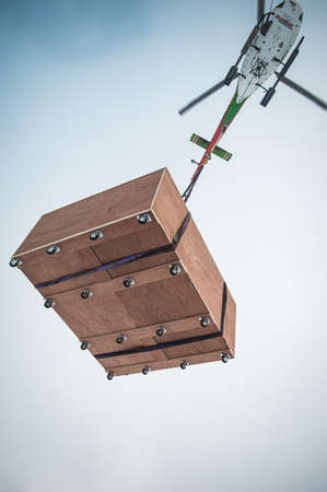 Picture of helicopter pilot droping oc a delivery. white helicopter dropping off a wooden plywood box.のeditorial素材
