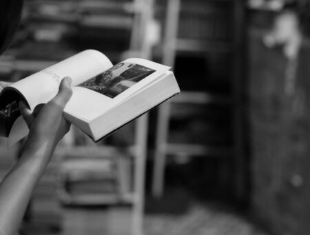 BLACK AND WHITE PHOTO OF GIRL READING BOOK SHOT FROM HER BACKの写真素材