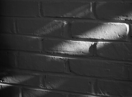 BLACK AND WHITE PHOTO OF NATURAL LIGHT ON WHITE PLAIN BRICK WALLの写真素材