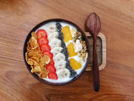 A bowl of flakes, grains, pecans, yogurt, oat, sliced strawberries and bananas