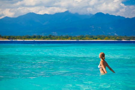 A beautiful woman wearing  white bikini facing the sea on a vacant beach in paradiseの写真素材