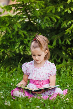 A little girl is  reading on the grassの写真素材