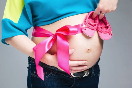 Pregnant belly with pink ribbon. Third trimester.の写真素材