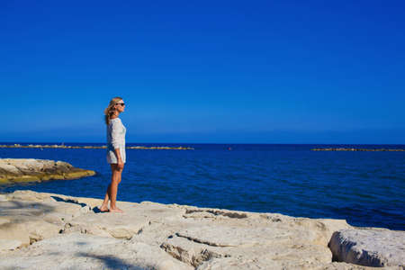 A beautiful girl stands on the rocky shore of the Mediterranean Sea Cyprus.Cheerful girl rests on...
