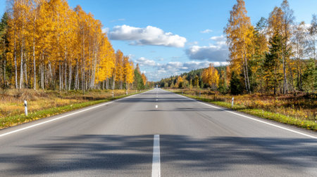An empty road stretches through a stunning autumn landscape adorned with golden trees and a bright blue sky, perfect for travel and exploration.の素材