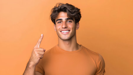 A joyful young man with stylish hair is smiling and pointing upward against a vibrant orange background. His positive energy radiates confidence and charm.の素材