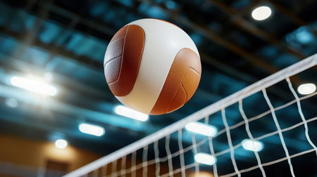 A spectacular shot of a volleyball soaring above a white net in an indoor sports facility, capturing the excitement and energy of the game in action.の素材