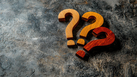 A vibrant arrangement of wooden question marks in orange and red on a textured gray background, evoking curiosity and reflection. Perfect for concepts of inquiry.の素材