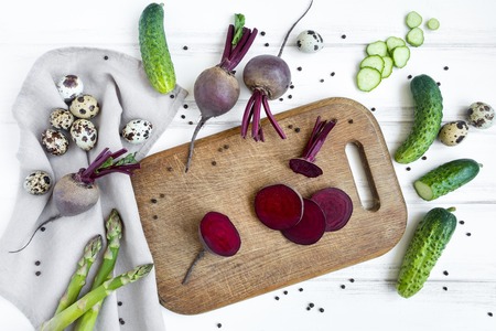 Sliced circles of beetroot on wooden cutting board, surrounded with vegetables and eggs. Home cooking concept. Salad or any vegetarian dish. Flat lay, top viewの写真素材