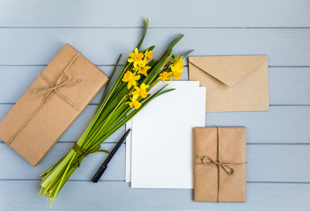 Letter, envelope, gifts in eco paper and daffodils bouquet on grey wooden background. Wedding invitation cards or love letter. Romantic holiday concept, top view, flat lay, overhead viewの写真素材