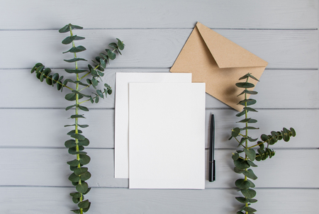 Letter, envelope and couple of fresh eucalyptus branches on grey wooden table. Wedding invitation card or letter with bright branches. Romantic or business concept, top view, flat layの写真素材