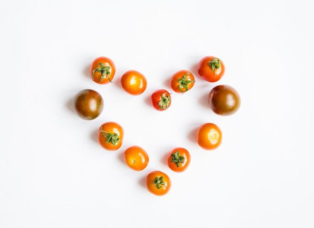 Bright cherry tomatoes in a heart shape on white background. Healthy food for salad. Flat lay, top view, view from aboveの写真素材