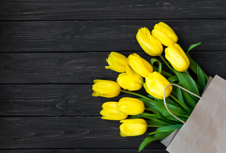 Bright yellow tulips in eco paper bag on black vintage wooden table. Flat lay, top view. Spring, shopping, eco conceptの写真素材