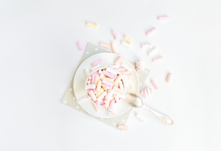 Colorful light marshmallows in a white cup with a spoon on white background. Light soft composition, sweet food concept. Top view, flat layの写真素材