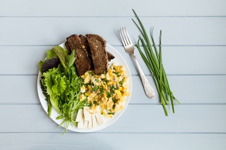 Homemade healthy breakfast: whole wheat dark toasted bread, scrambled eggs, cheese, green salads. Flat lay, top view on grey wooden table, decorated with onionsの写真素材