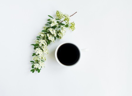 Cup of black coffee and beautiful white flowering Spirea arguta (brides plant) branch on white table. Flat lay, top view, space for text. Romantic home compositionの写真素材